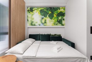 A modern bedroom with a bed, pillows, and a large window with a green leaf painting. - Global Park Superior Studio (Katowice)