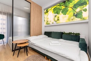 Quarto moderno com uma cama, uma mesa de madeira redonda e uma janela grande com persianas.