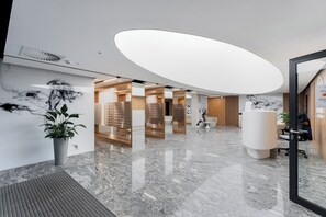 A modern lobby with a marble floor, a reception desk, and a large, oval-shaped light fixture. - Global Park Superior Studio (Katowice)