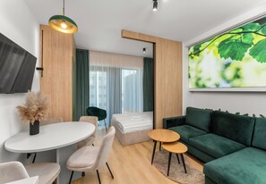 Uma sala de estar moderna com um sofá verde, uma mesa de jantar redonda e uma janela grande com cortinas.