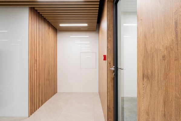 Um corredor com painéis de madeira em uma lateral, piso de azulejos e uma porta com painel de vidro na outra.