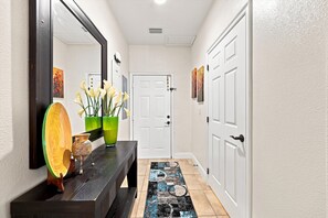 A hallway with a dark wooden bench, a mirror, a vase with flowers, and a patterned rug. - Sleep 8 Near Disney | FREE Resort & Pool Access (Davenport)