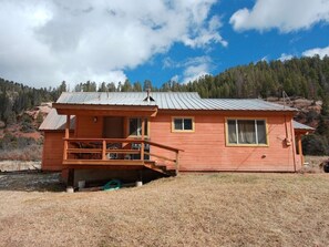 A wooden cabin with a porch, windows, and a metal roof, set against a mountainous backdrop. - Three Bedroom Cabin Escape near Dolores River on Private 300 Acre Ranch! (Dolores)