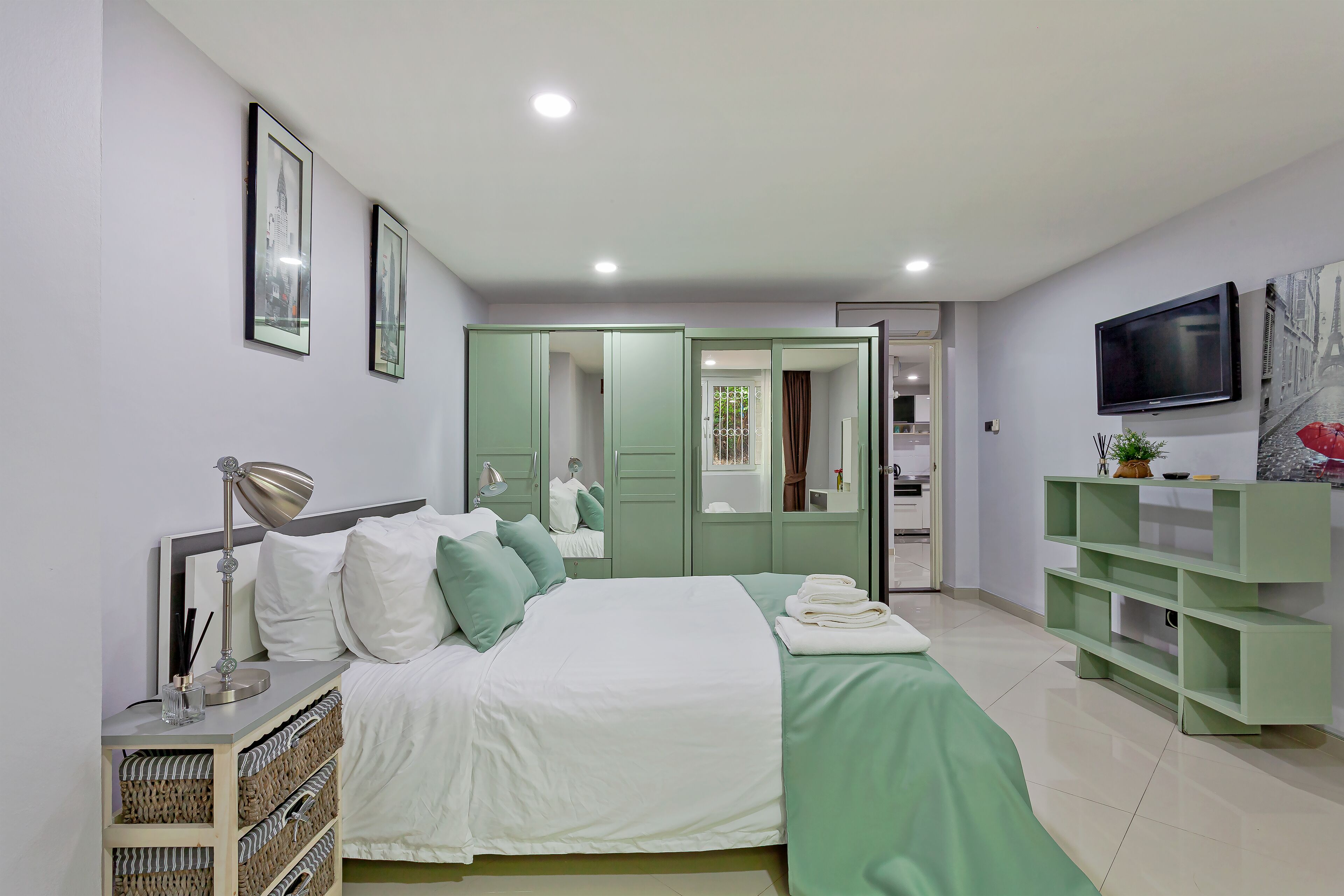 A modern bedroom with a bed, bedside lamp, and a TV mounted on the wall.