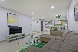 Ein modernes Wohnzimmer mit Flachbildfernseher, Glastisch, Sofa und Essbereich im Hintergrund.