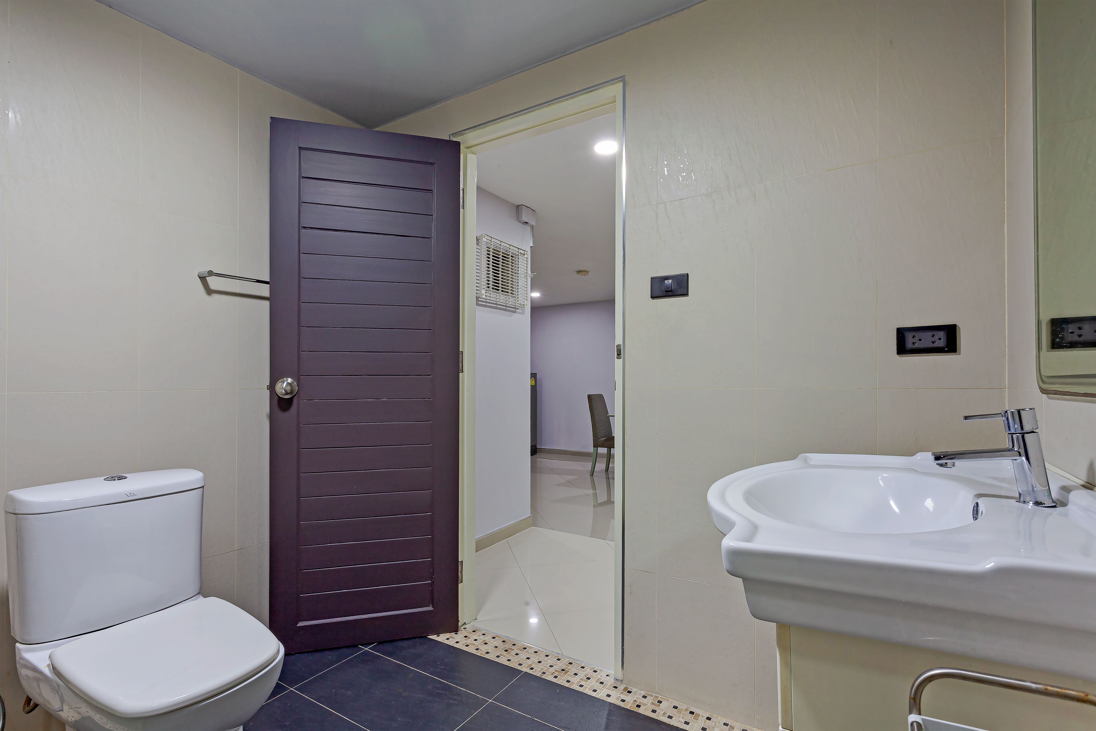 A bathroom with a toilet, a sink, and a door leading to another room.