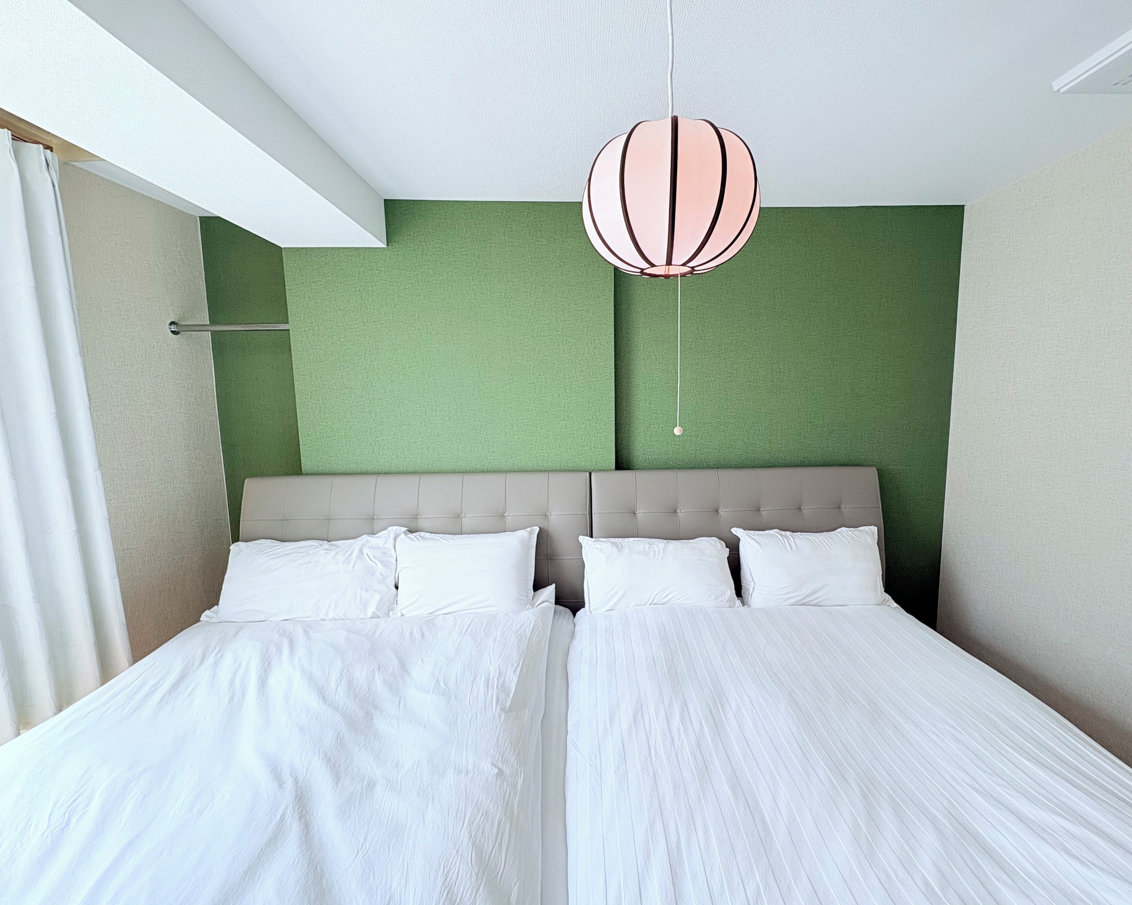 A double bed with white linens in a room with green walls and a beige headboard.