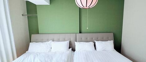 A double bed with white linens in a room with green walls and a beige headboard.