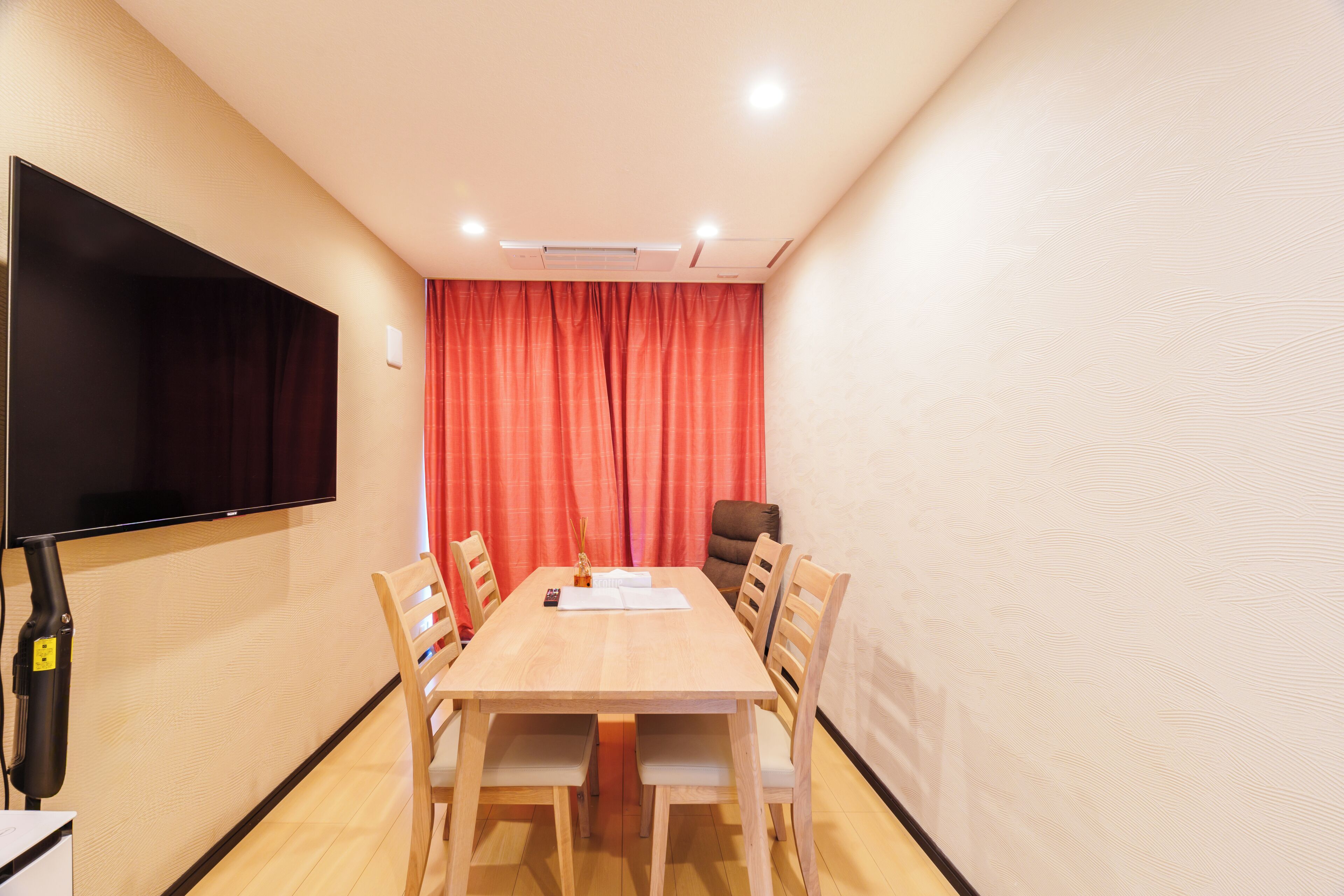 Una sala de conferencias con una mesa de madera, seis sillas, un televisor de pantalla plana y cortinas rojas.
