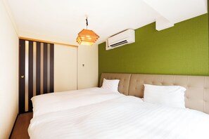 Quarto de hotel com cama, ar condicionado fixado na parede, porta listrada e luminária pendente.