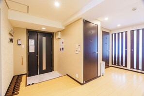 Corredor de hotel com um sapateiro, portas duplas e um cesto de lixo.