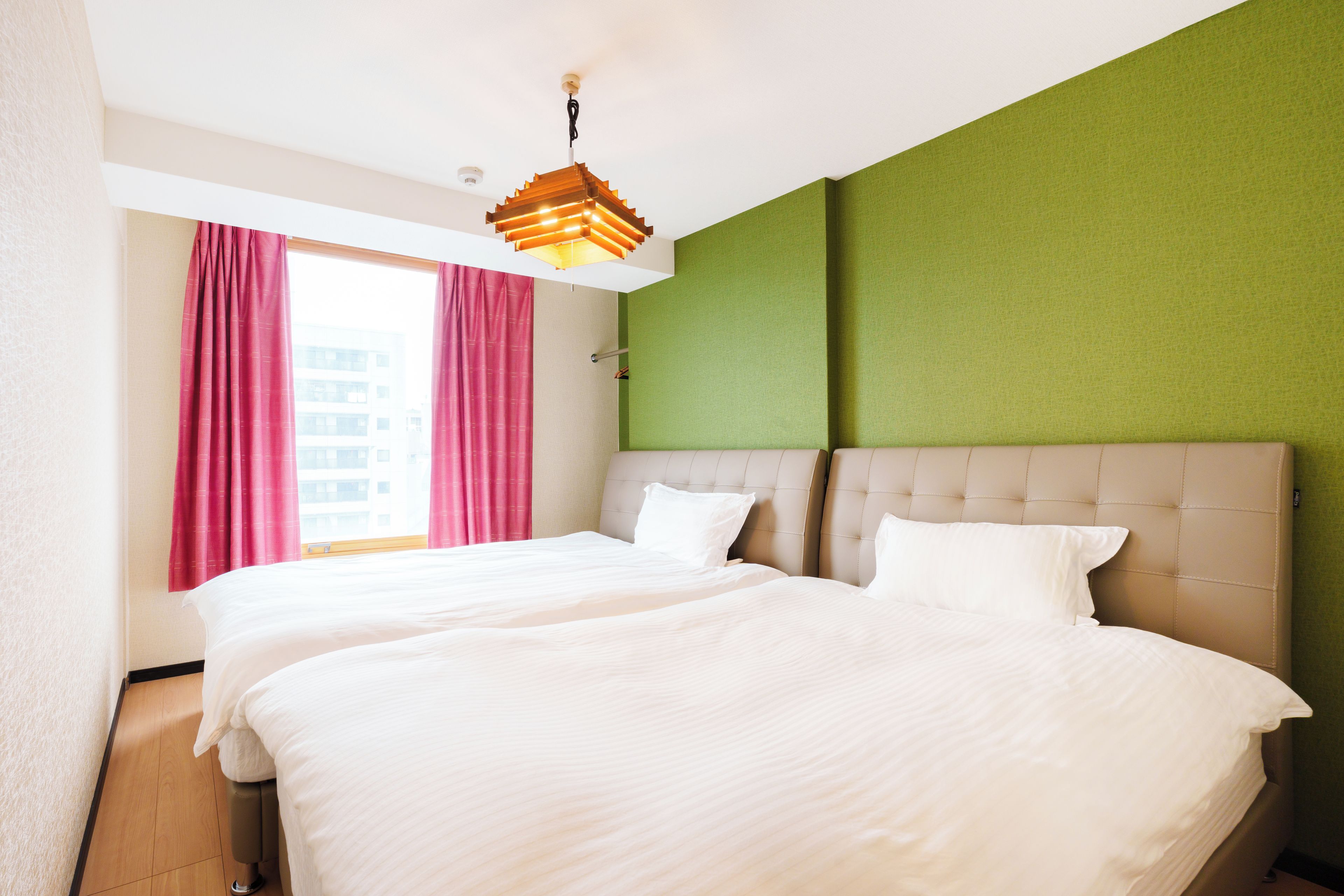 A hotel room with a large bed, a window with curtains, and a unique ceiling light fixture.