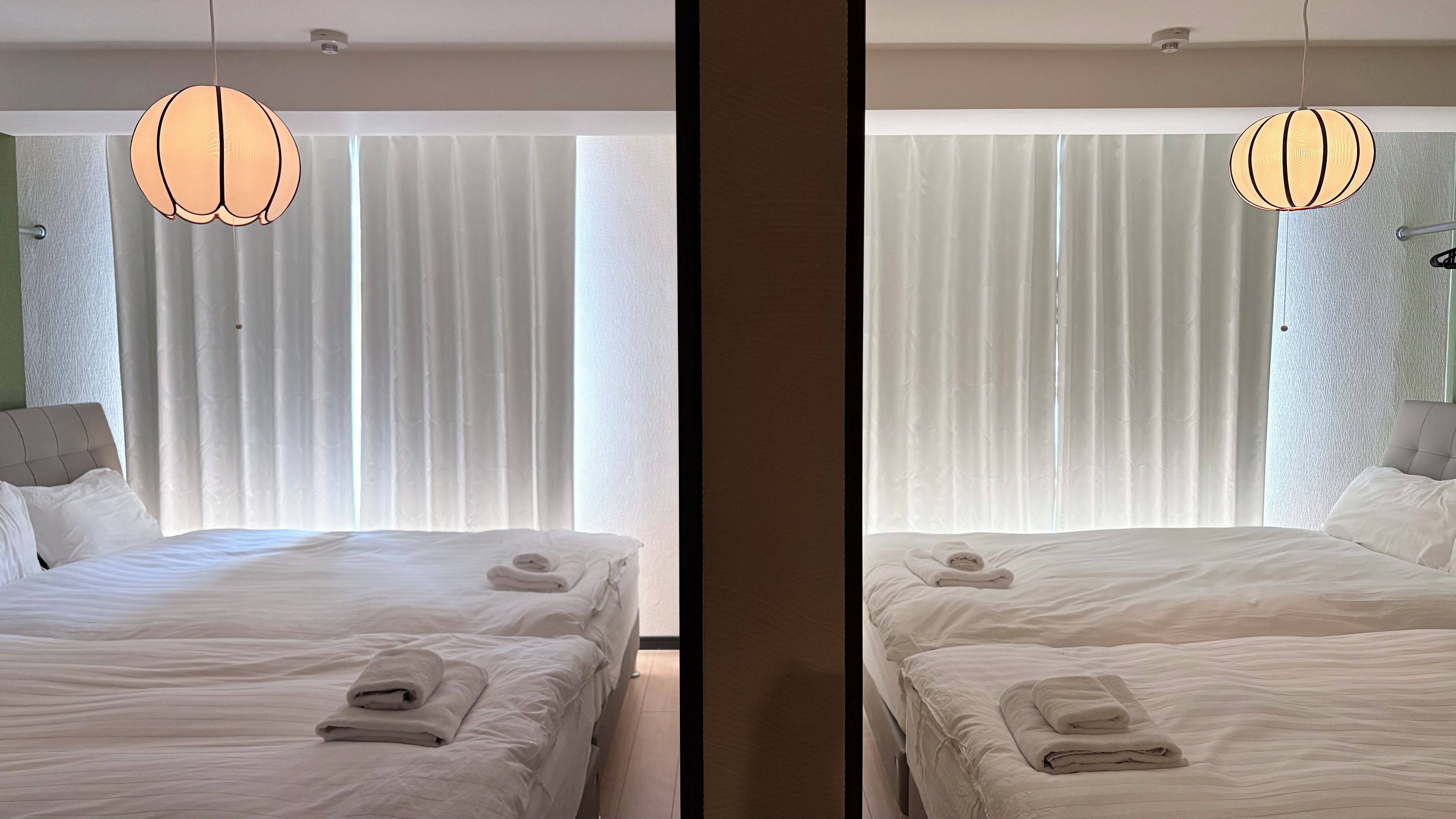 Habitación de hotel con dos camas, un ventanal con cortinas y una lámpara colgante.
