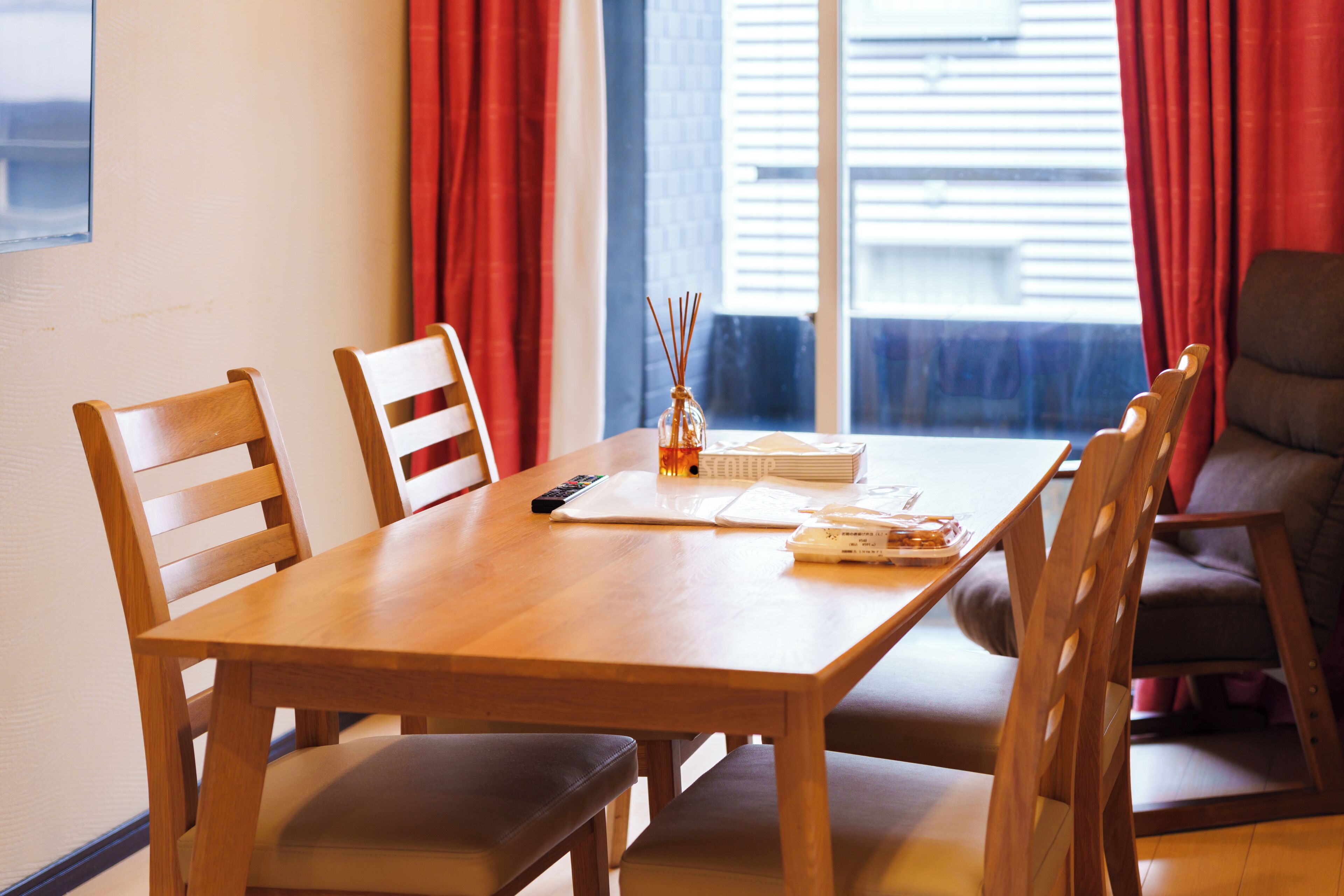 A wooden dining table with four chairs, a remote control, a notebook, and a glass container with sticks.
