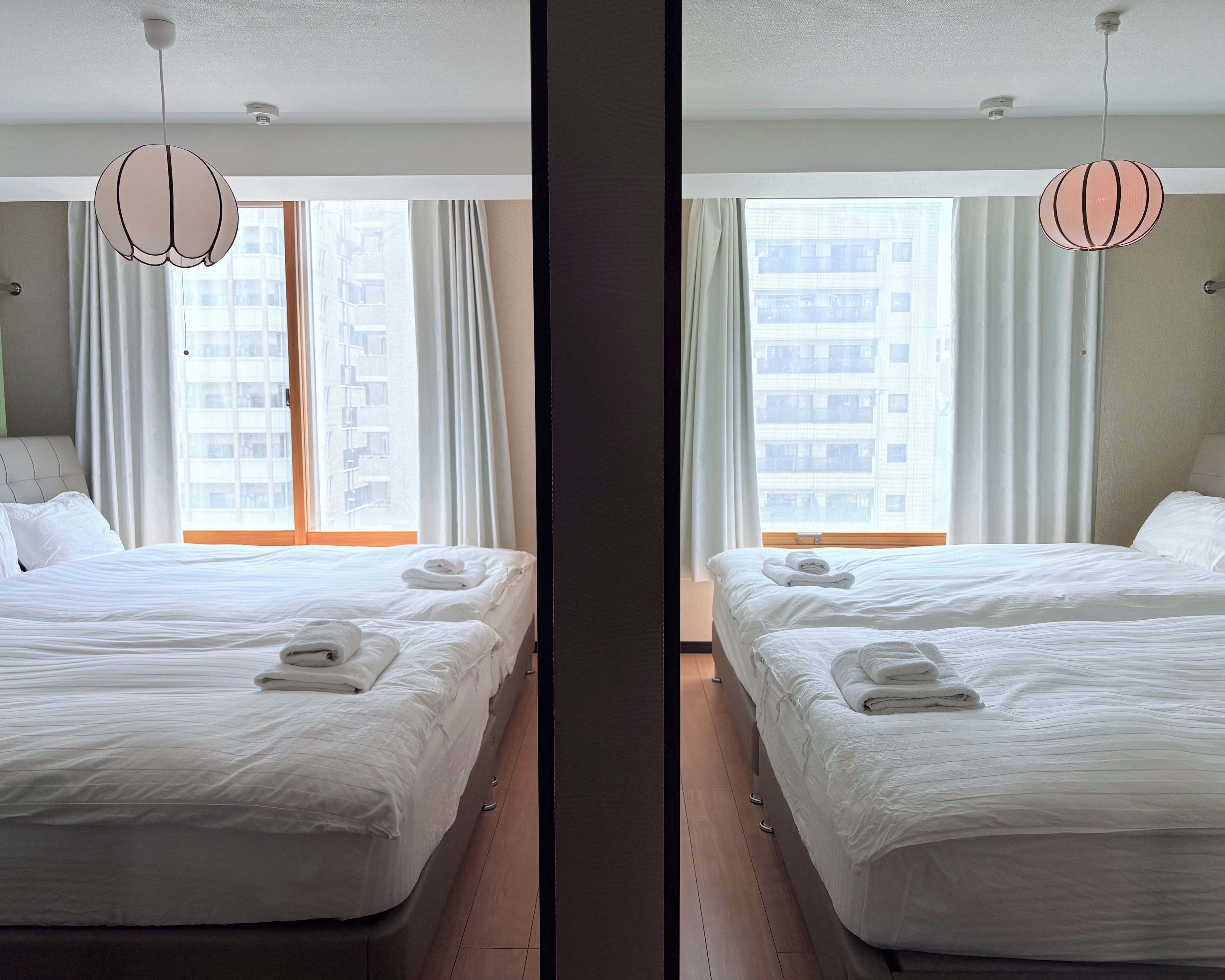Een hotelkamer met twee bedden, witte lakens, uitzicht op een gebouw door het raam en een hanglamp.
