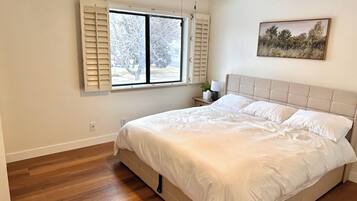 A bedroom with a bed, a window with shutters, a ceiling fan, and a painting on the wall.