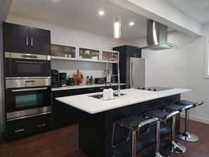 A modern kitchen with a central island, bar stools, stainless steel appliances, and a pendant light.