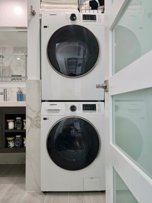 A stacked washer and dryer unit in a modern kitchen with marble countertops and a glass door.