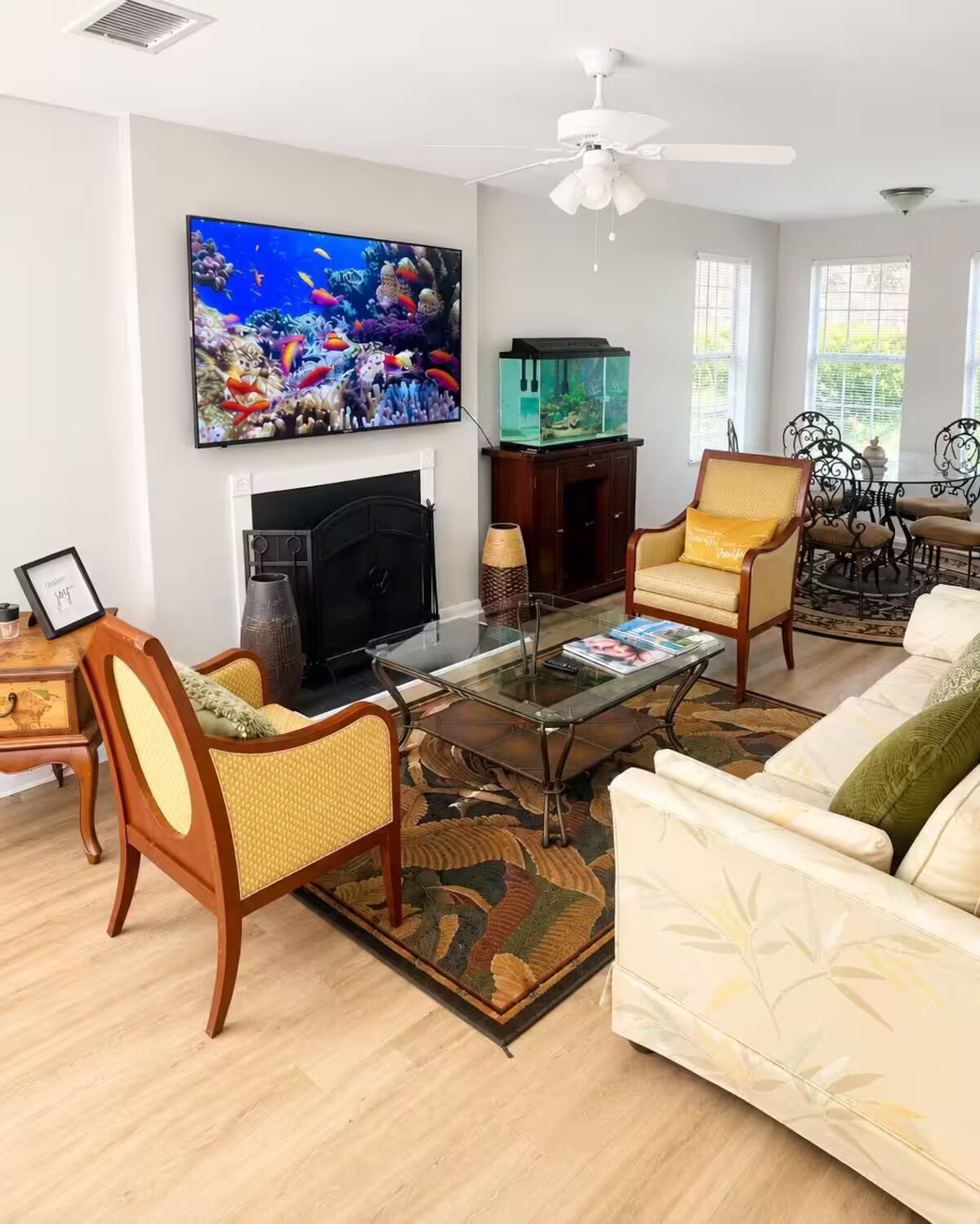 A living room with a fireplace, a television, a fish tank, and a dining area with metal chairs.