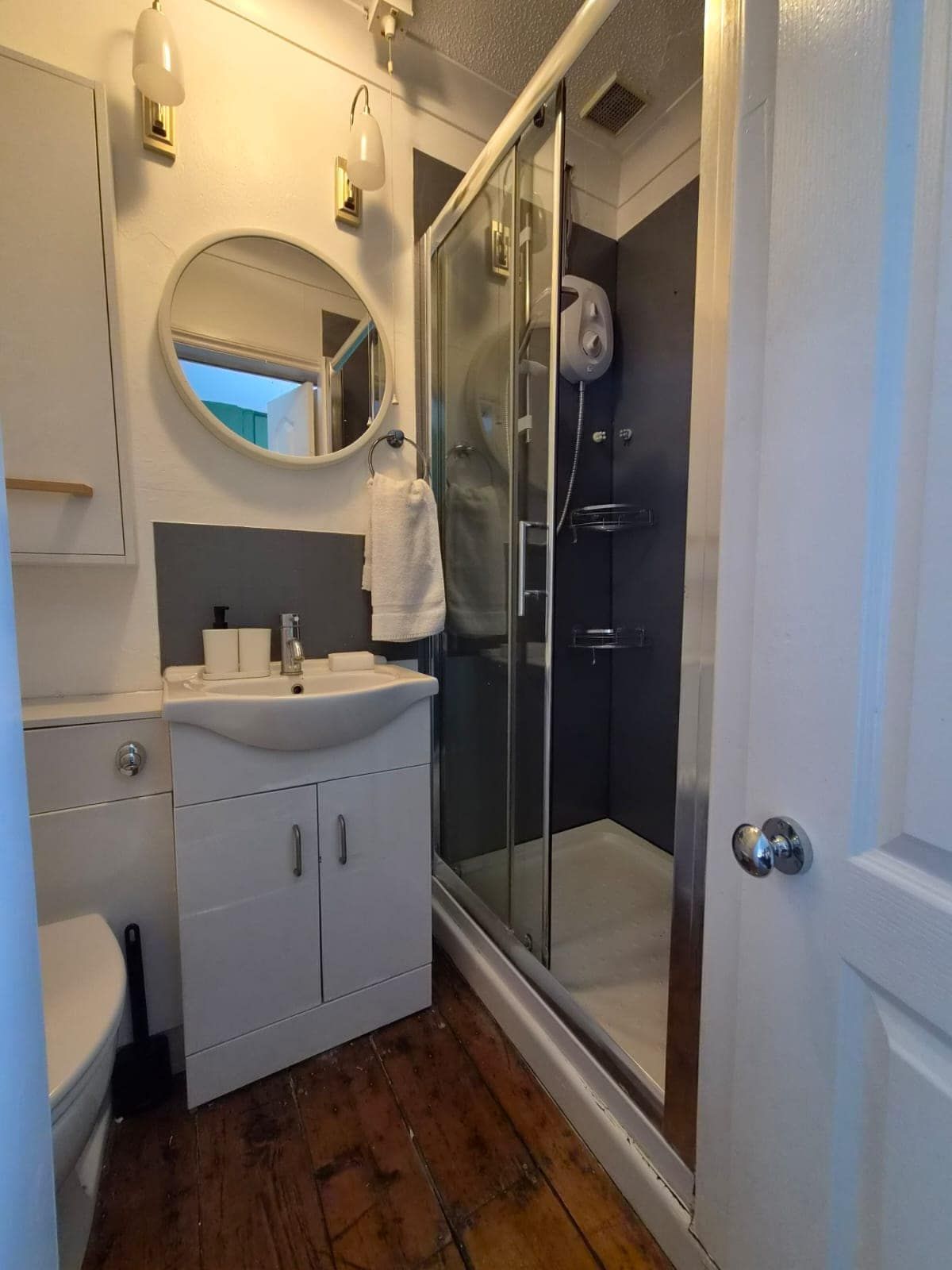 Un baño con lavamanos blanco, espejo y ducha con mampara de vidrio.