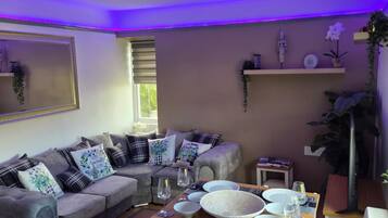 A dining area with a table set for four, a sofa, and a window with blinds.