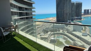 A balcony with a view of a coastal cityscape, including modern high-rise buildings and a beach. - Luxury 1-bedroom in Gate tower with double View (New Alamein)