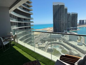 Ein Balkon mit Blick auf eine Küstenstadtlandschaft, darunter moderne Hochhäuser und ein Strand.