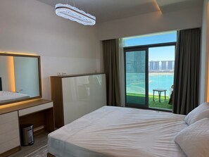 Ein Hotelzimmer mit Bett, Nachttisch, Spiegel, Mülleimer und einem großen Fenster mit Blick auf ein Gewässer und Gebäude.