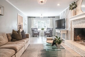 Uma sala de estar com sofá, poltronas, mesa de centro, televisão e lareira.