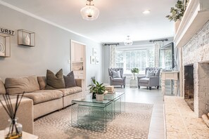A modern living room with a sofa, armchairs, a glass coffee table, and a fireplace. - The Mad Hatter Inn - In the Village of Pinehurst! (Pinehurst)