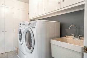 A compact laundry area with a front-loading washing machine and a sink. - The Mad Hatter Inn - In the Village of Pinehurst! (Pinehurst)