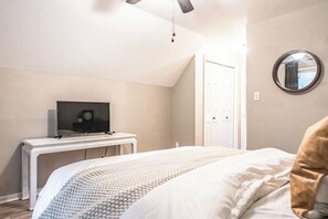 A bedroom with a bed, a bedside table with a television, a ceiling fan, and a door. - The Mad Hatter Inn - In the Village of Pinehurst! (Pinehurst)
