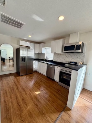 A modern kitchen with white cabinets, stainless steel appliances, and a wooden floor. - Golden safari home Perfect Getaway for Relaxation (Tampa)