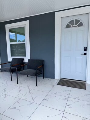 A house exterior with a white door, a window, and two chairs outside. - Golden safari home Perfect Getaway for Relaxation (Tampa)