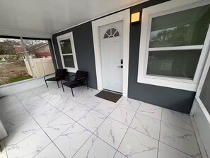 A covered porch with two chairs, a white door, and large windows. - Golden safari home Perfect Getaway for Relaxation (Tampa)