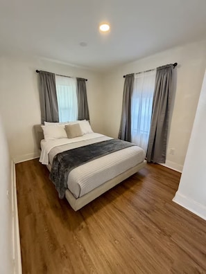A bedroom with a bed, curtains, and a wooden floor. - Golden safari home Perfect Getaway for Relaxation (Tampa)