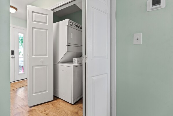 Un lavadero con lavadora y secadora, una cesta y una puerta que da a otra habitación.