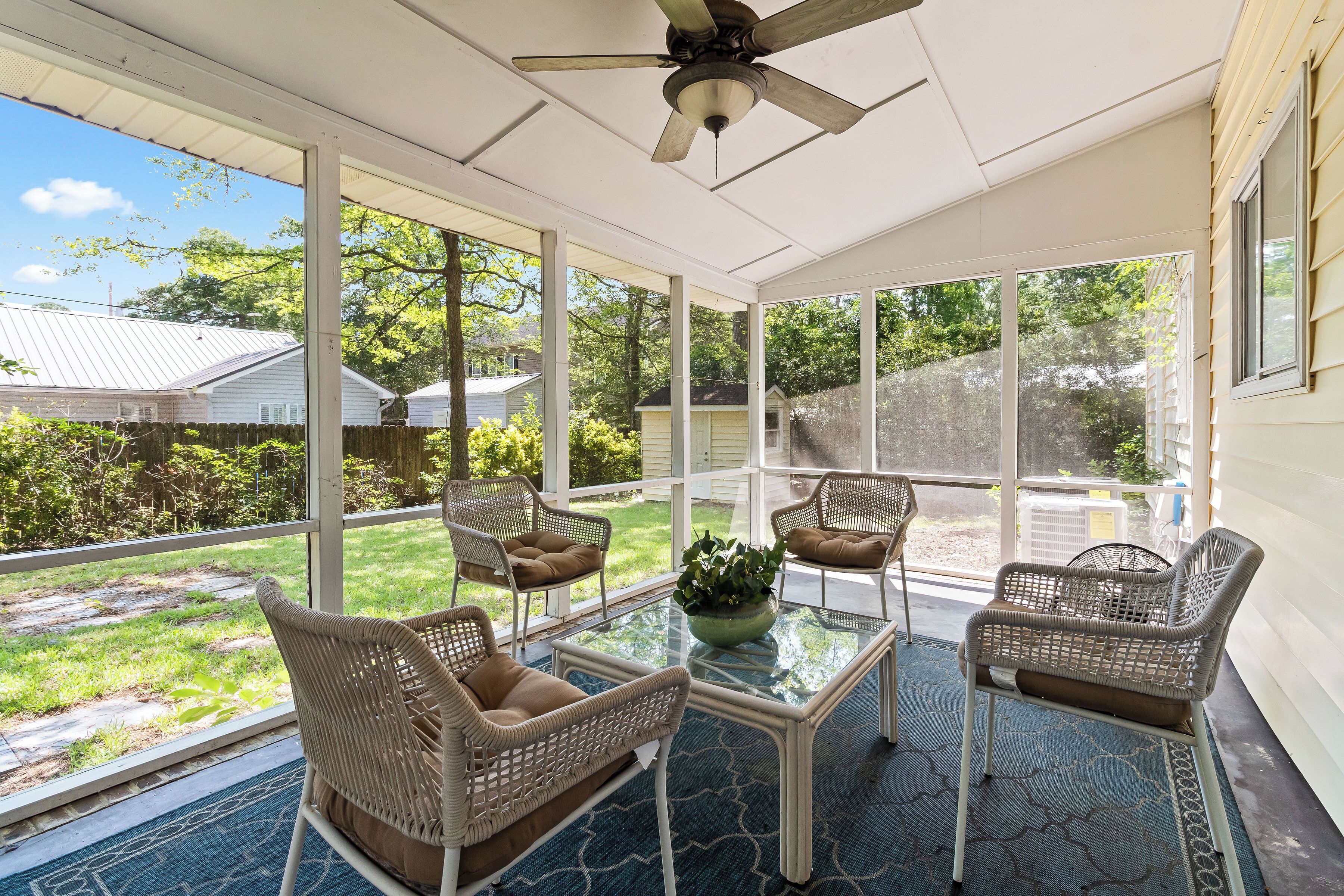A sunroom with wicker furniture, a ceiling fan, and large windows offering a view of the backyard.