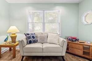Ein Wohnzimmer mit einem beigen Sofa, Kissen mit Muster, einer Lampe und einem Beistelltisch.