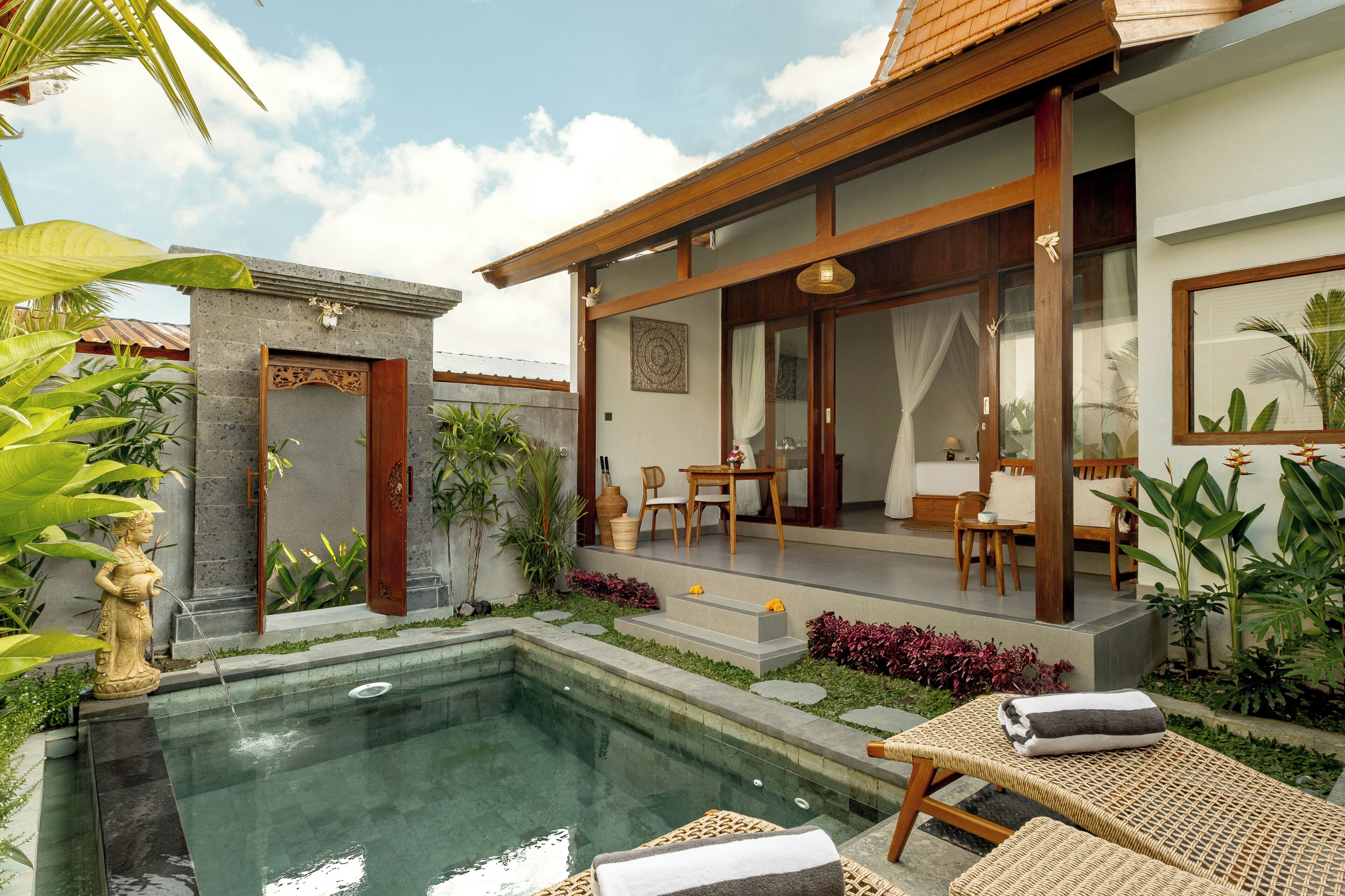 Un área de piscina con sillones reclinables, un comedor con mesa y sillas, y una pared de piedra con una puerta decorativa.