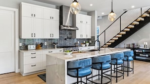 A modern kitchen with white cabinets, a central island with bar stools, and a staircase leading to another level. - River Bend by Avantstay Private Pool + Hot Tub + Game Room Hill Country Views (Austin)