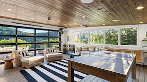 Une pièce spacieuse avec un grand plafond en bois, une table de ping-pong et une vue sur un paysage montagneux grâce à de grandes fenêtres.