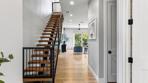 En modern inredning med en trappa i trä, en hall som leder till ett rum med utsikt och en dörr med en mönstrad gardin.