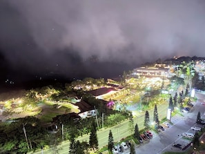 A nighttime aerial view of a town with illuminated buildings, a parking area, and a road.