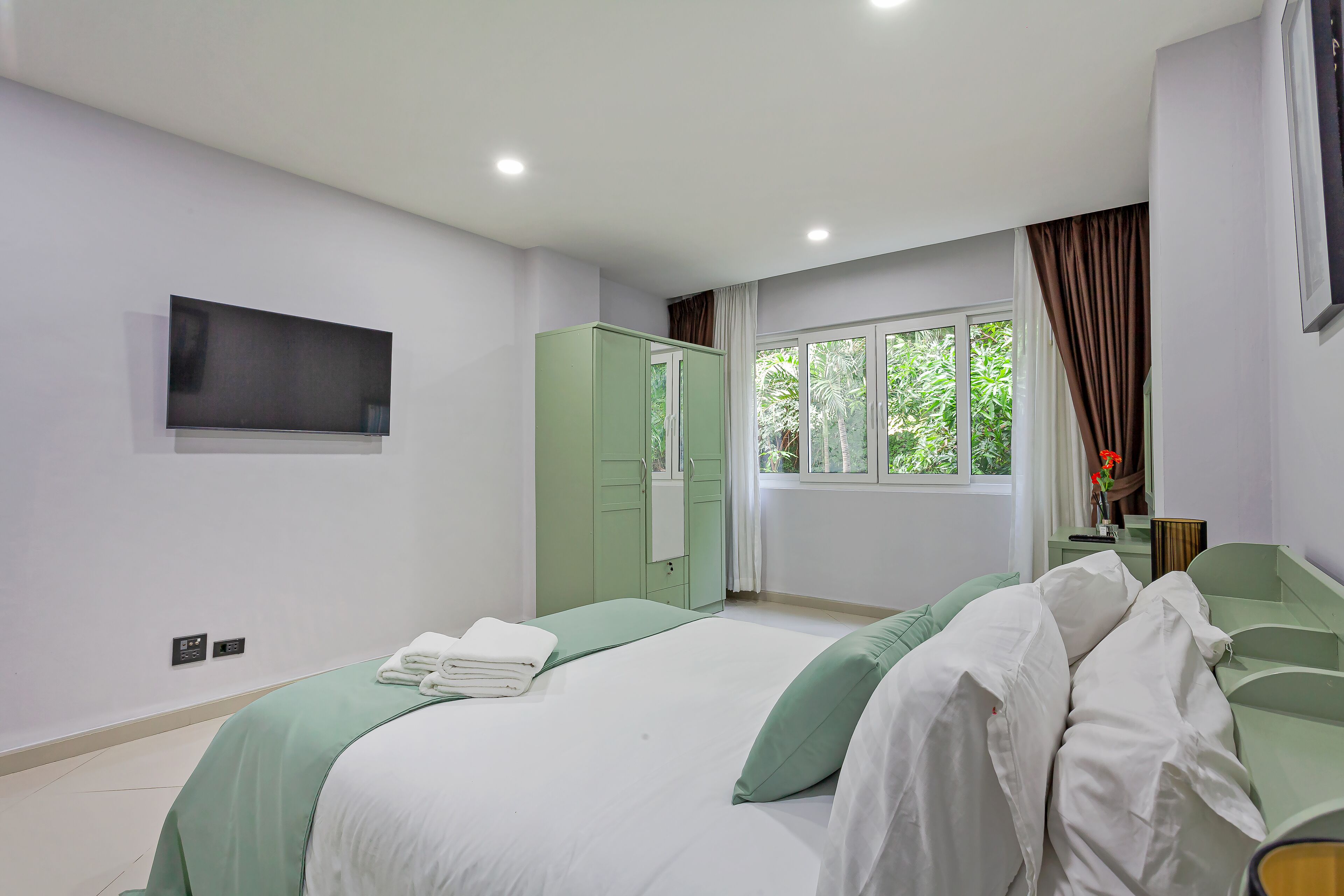 Une chambre à coucher avec un lit, une armoire, une télévision et une fenêtre avec des rideaux.