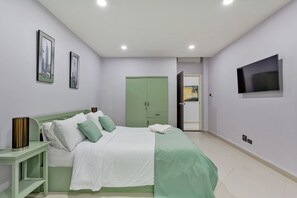 A bedroom with a bed, a nightstand, a wardrobe, a painting, and a television. - The 1 Bedroom "Three" Apartment - Olympic Pool (Muang Pattaya)