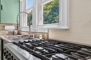 Una cocina con estufa a gas, un lavamanos y una ventana con vistas a la vegetación.