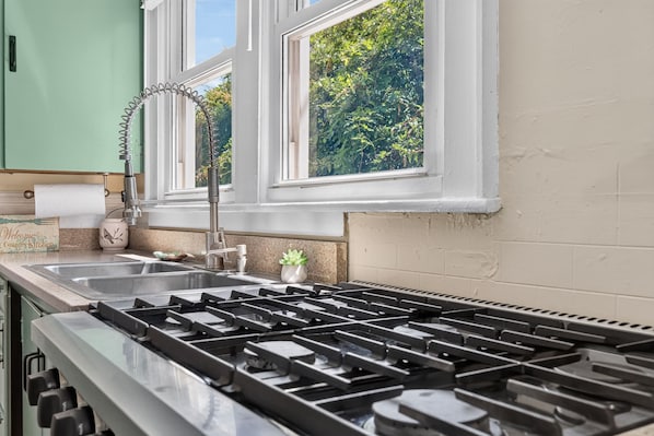 A kitchen with a gas stove, a sink, and a window overlooking greenery.