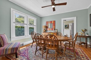 A dining room with a round table, wooden chairs, a ceiling fan, and a large window with blinds. - Side Street Bungalow -Close to Town/Shopping/Tryon Equestrian Center/Restaurants (Forest City)