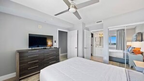 Une chambre d’hôtel avec un grand lit, un téléviseur posé sur une commode, un ventilateur de plafond et une vue sur l’extérieur.